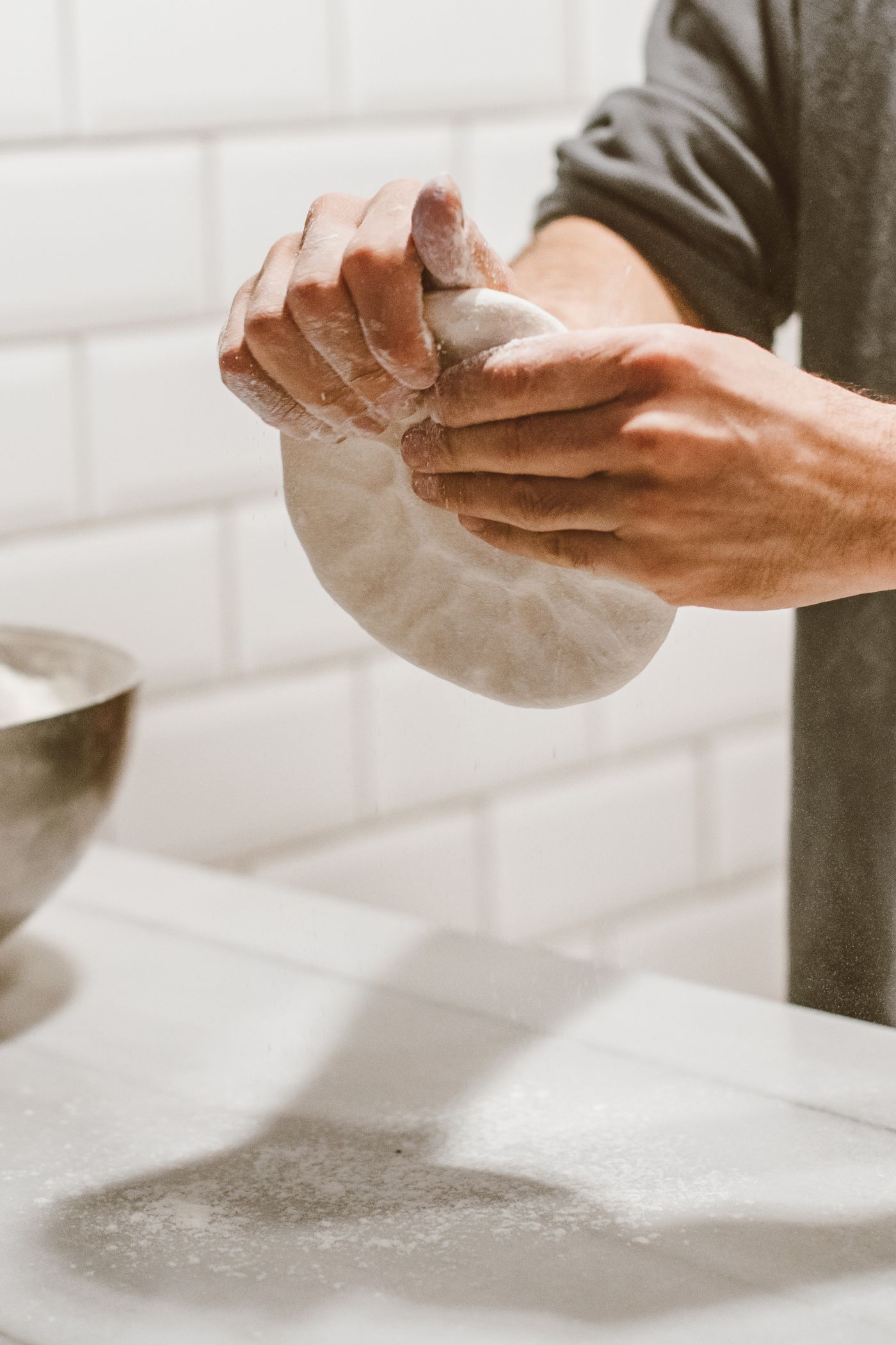 Floured hands working a round of dough on a kitchen worktop